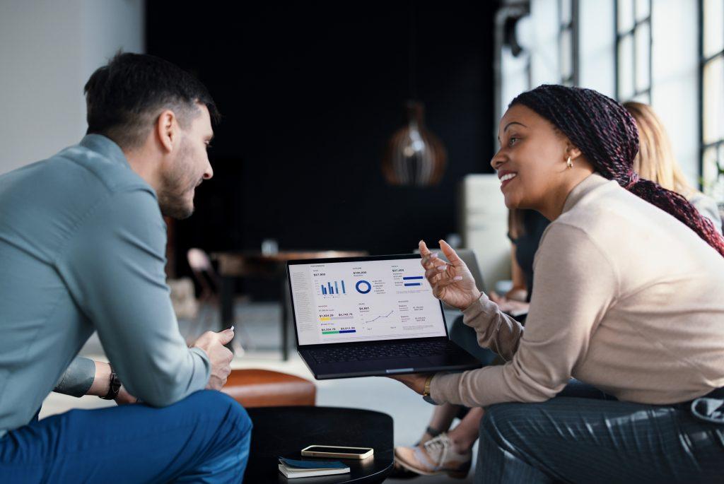 A professional business team collaborates, analyzing data presented on a laptop screen in a modern, bright office setting, fostering teamwork, productivity, and aligning on strategies for business success.